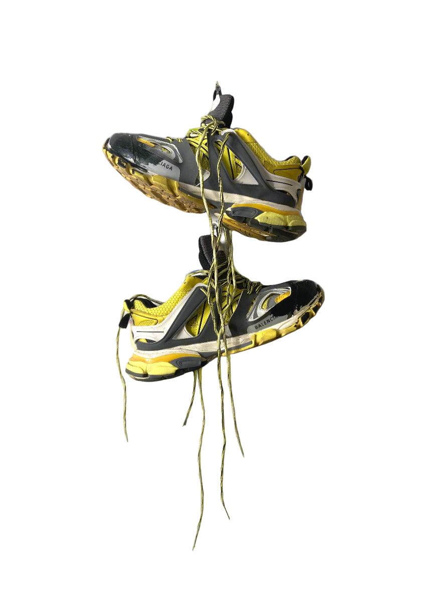 Pair of black and yellow sneakers hanging against a gray background